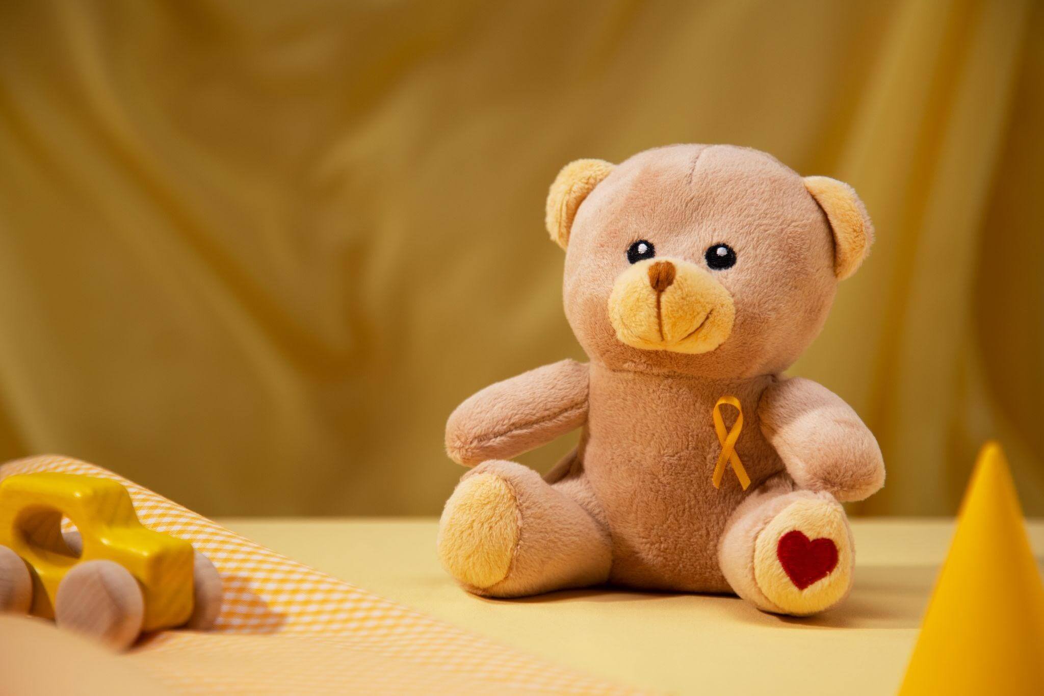 Uso de pelúcia com uma fita dourada, símbolo do combate e conscientização contra o câncer infanto-juvenil.