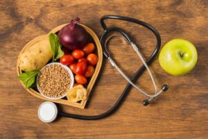 Prato em forma de coração, repleto de alimentos para prevenir doenças cardíacas. Ao lado, um estetoscópio e uma maçã verde destacam a importância de uma dieta saudável para a saúde do coração.