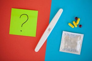 Teste de gravidez centralizado a imagem. De um lado um papel com ponto de interrogação e outro alguns métodos contraceptivos, simbolizando dúvidas sobre o assunto.
