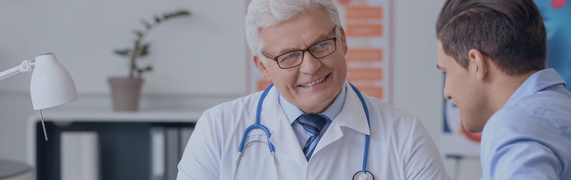 Médico sorridente conversa com paciente durante consulta de rotina, representando o cuidado integral e a importância da prevenção na saúde do homem durante o Novembro Azul.