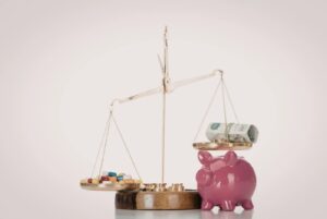 Balança de um lado com medicamentos e o outro com uma nota de dinheiro e um cofre de porquinho